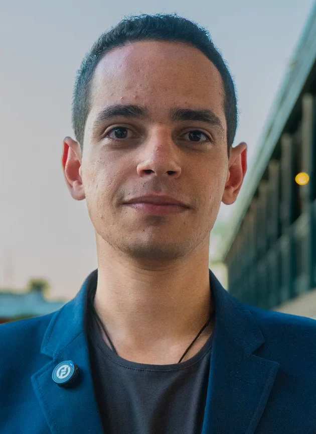 Daniel Sodré, profissional de marketing digital e CEO da New Arrays, vestindo blazer azul e posando com confiança em ambiente urbano ao ar livre